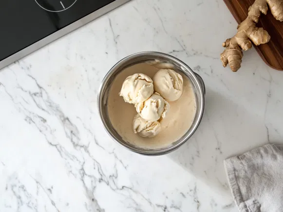 The ginger ice cream is shown transferred to a container on the white marble cooktop, ready to be placed in the freezer to firm up before scooping and serving.