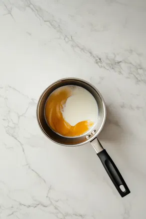 A medium saucepan on the white marble cooktop holds butter and light brown sugar melting over medium heat. Double cream, vanilla extract, and black treacle are stirred in, and the mixture is brought to a gentle boil, creating a rich, golden toffee sauce.