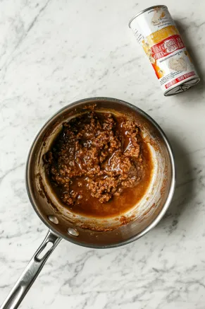 A saucepan on a white marble cooktop with butter and brown sugar bubbling together to create caramel, with a can of condensed milk placed beside the pan.