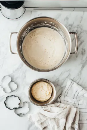 A large stockpot on the white marble cooktop with metal cookie cutters or a towel at the bottom to elevate the pudding mold. Water is boiling in the pot. Nearby, a 1.6-liter pudding mold is greased and ready for the batter.