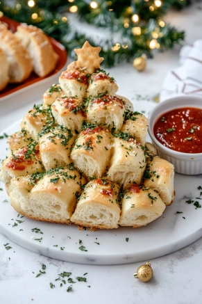 The festive pull-apart Christmas tree bread sits on a decorative platter on the white marble cooktop. A small bowl of warm marinara sauce is placed nearby for dipping, completing the inviting presentation.