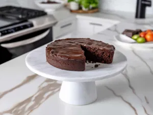 The completed gluten-free chocolate fudge cake on a cake stand on the white marble countertop, beautifully sliced and ready to be served.