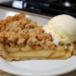 A warm slice of apple crumb pie is served on a dessert plate, placed on the white marble cooktop. A scoop of vanilla ice cream melts over the pie, creating an enticing dessert presentation.