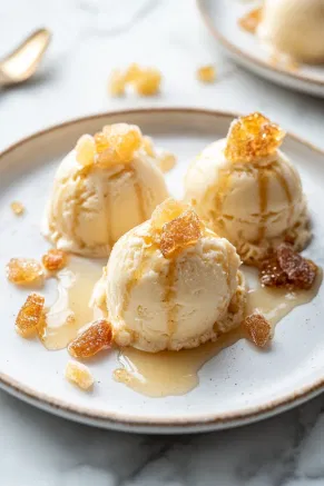 The frozen ginger ice cream desserts unmolded onto a plate on the white marble countertop, garnished with crystallized ginger and drizzled with ginger syrup for an elegant presentation.