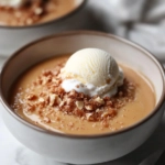 A serving of warm butterscotch pudding is shown in a bowl on the white marble cooktop, topped with a scoop of vanilla ice cream, ready to be enjoyed.