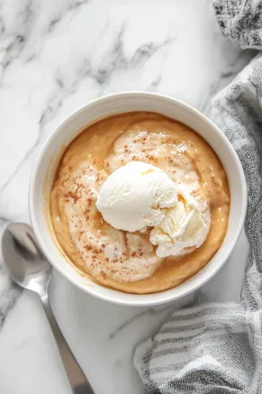 A serving of warm butterscotch pudding is shown in a bowl on the white marble cooktop, topped with a scoop of vanilla ice cream, ready to be enjoyed.