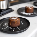 Warm salted caramel chocolate fondants served on black plates on the white marble cooktop, the rich, molten centers ready to enjoy.