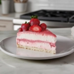 A slice of Strawberry Delight is served on a plate over the white marble cooktop, showcasing its colorful layers and creamy texture.