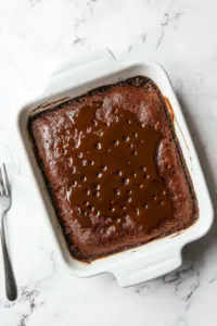 Baked pudding cooling on a white marble cooktop with small holes poked across the surface, soaking in warm toffee sauce for added flavor.