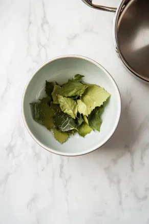 On the white marble cooktop, a bowl holds gelatine leaves soaking in cold water. A small pot nearby simmers, ready to dissolve the softened gelatine, which will then be set aside to cool before use.