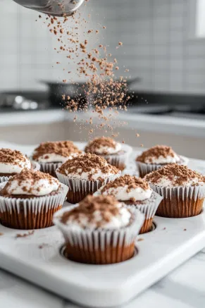 Crushed cookie crumbs being sprinkled over the filled muffin cups on the white marble cooktop, prepared for baking.