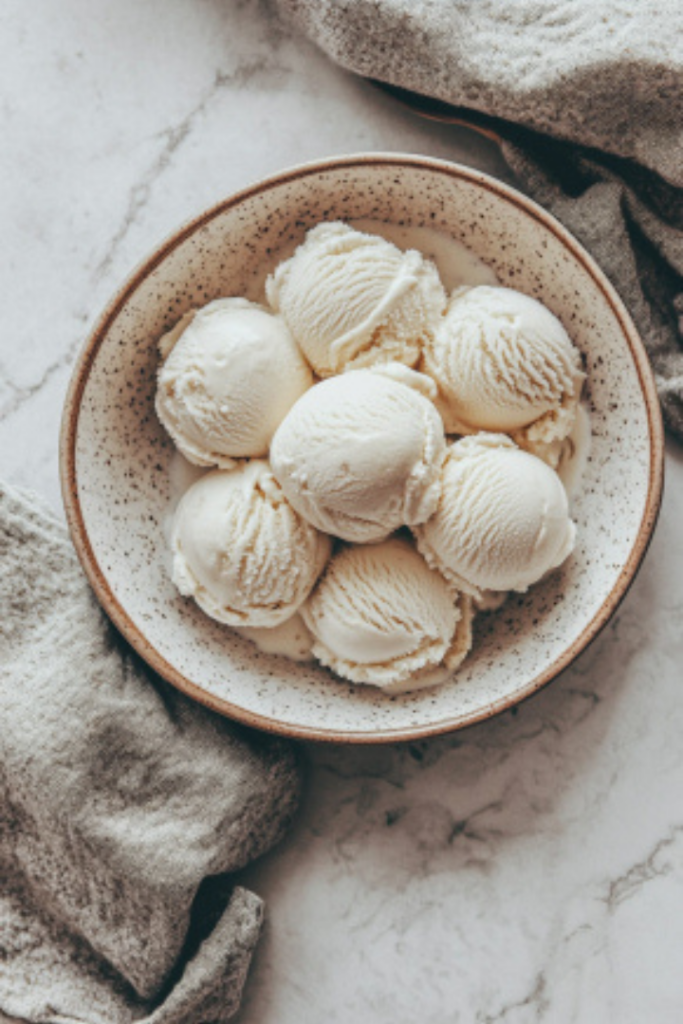 Scoops of frozen vanilla ice cream served in a bowl on the white marble countertop, ready to be enjoyed as a delicious treat.