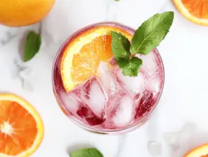 A glass of layered fruit punch served over ice with slices of orange, lemon, and lime, garnished with apple pieces, ready to enjoy