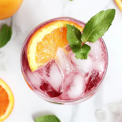 A glass of layered fruit punch served over ice with slices of orange, lemon, and lime, garnished with apple pieces, ready to enjoy