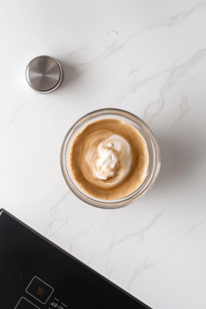 The completed Dalgona Coffee on the white marble cooktop, with its velvety whipped coffee topping sitting over the milk and ice. Ready to stir and enjoy!