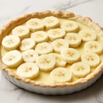 The assembled banana custard pie being placed in the preheated oven. It bakes for 12 to 15 minutes until the filling is set.