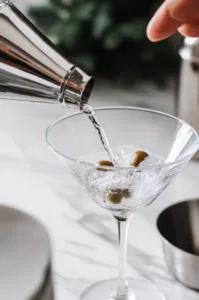 A spoon stirring the ingredients in the mixing glass on the white marble cooktop, ensuring the vodka, vermouth, and brine are well combined for a smooth, salty flavor.