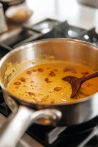 The saucepan on medium heat on the white marble cooktop as the golden milk mixture comes to a gentle simmer. It simmers for about 10 minutes, with occasional stirring to prevent sticking, allowing the flavors to meld.