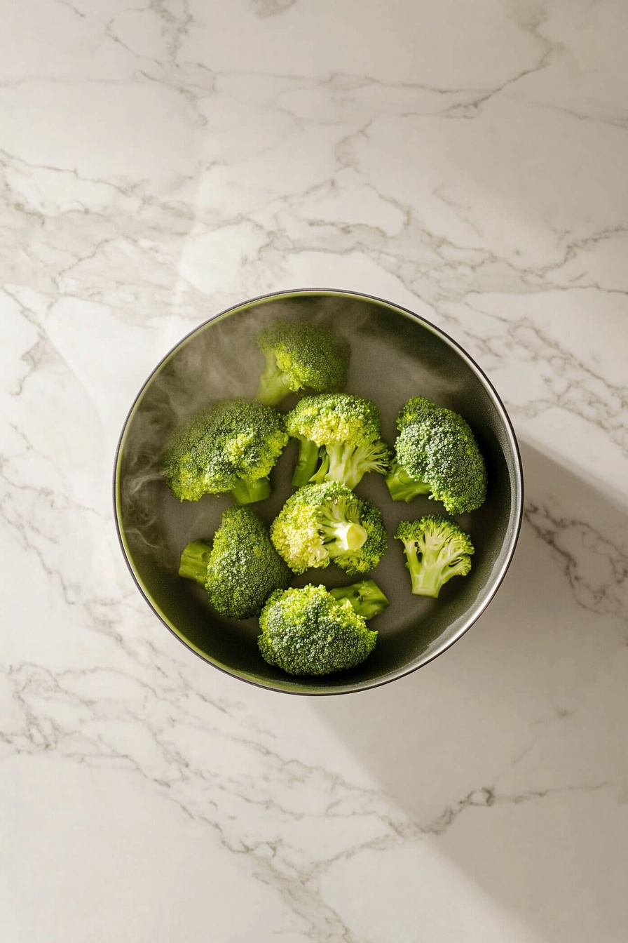 Chicken broth is poured into the cast-iron skillet on the white marble cooktop, deglazing the pan. Golden-brown bits from the chicken dissolve into the broth, creating a flavorful base for the dish.