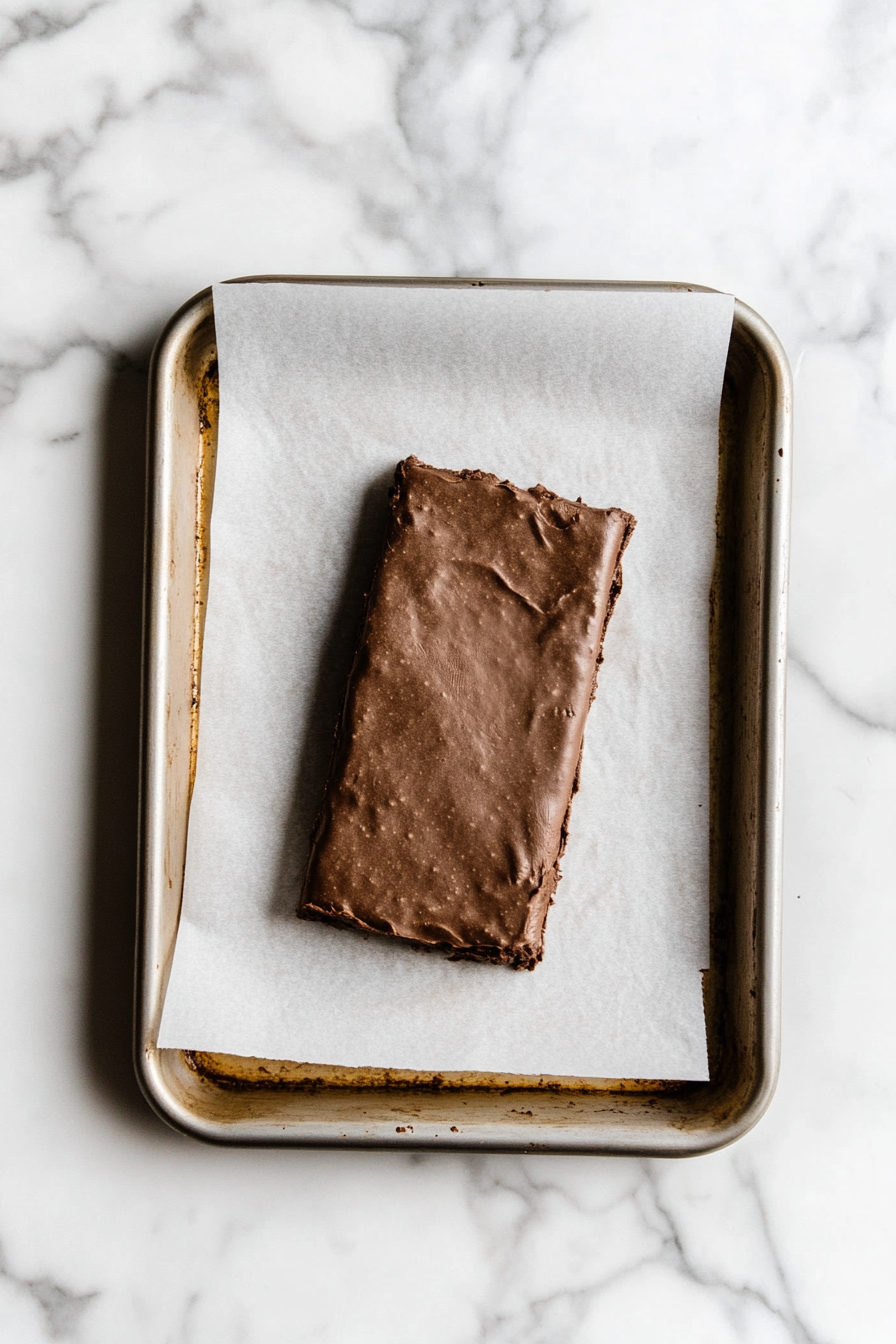 The dough rolled out between two sheets of parchment paper on the white marble cooktop. The dough is placed on a baking sheet, ready to be refrigerated for 1 hour