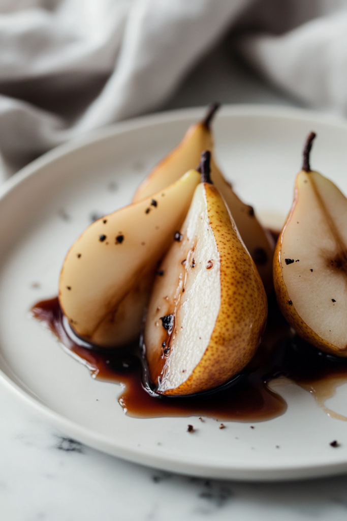 The black skillet on the white marble cooktop, with roasted pears resting briefly. The pears are slightly softened, their golden surfaces accented by honey and balsamic glaze, ready for serving