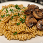 Close-up shot of a plate on the white marble cooktop with creamy vegan mushroom stroganoff. The pasta is garnished with fresh parsley and a sprinkle of vegan parmesan, ready to be served hot.