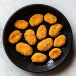 Close-up shot of a shiny black skillet on the white marble cooktop, holding the chilled vegan chicken tenders, ready to be seasoned and cooked. Their texture appears firm, with an even golden hue, perfect for pan-frying, grilling, breading, or slicing.