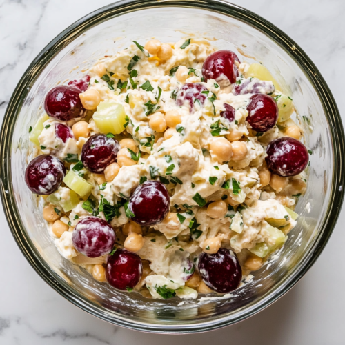 Close-up shot of the glass bowl on the white marble cooktop with the almond/chickpea mixture fully blended into a creamy salad, covered with plastic wrap, ready to be refrigerated