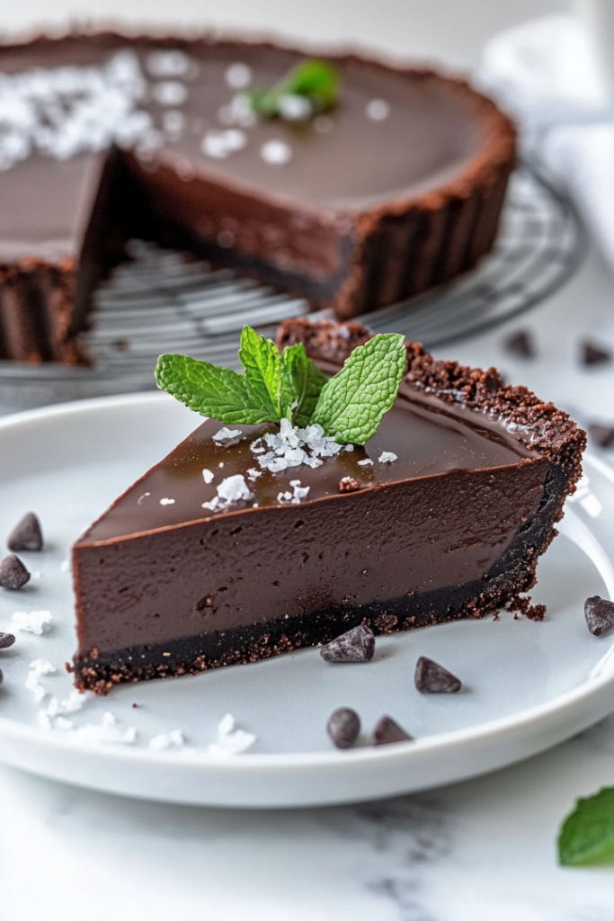 A close-up of the chilled tart on a white marble countertop, garnished with a sprinkle of flaky sea salt over the glossy chocolate surface for an elegant finish.