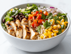 side view of a vibrant and colorful chicken bowl arranged on a white marble countertop. The bowl contains a bed of fluffy cilantro lime rice topped with perfectly grilled chicken thighs, sautéed green and red peppers, black beans, roasted corn, and a creamy sauce drizzle. The ingredients are arranged neatly, creating a flavorful, balanced meal that is visually appealing and fresh.