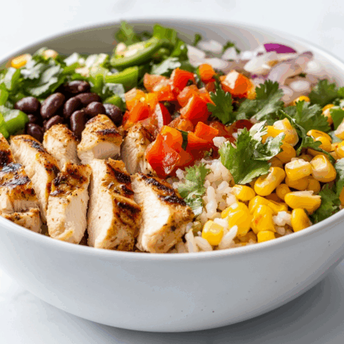 side view of a vibrant and colorful chicken bowl arranged on a white marble countertop. The bowl contains a bed of fluffy cilantro lime rice topped with perfectly grilled chicken thighs, sautéed green and red peppers, black beans, roasted corn, and a creamy sauce drizzle. The ingredients are arranged neatly, creating a flavorful, balanced meal that is visually appealing and fresh.