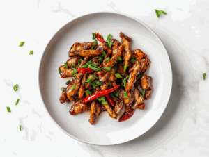 A delicious plate of crispy chilli chicken coated in a glossy, sticky sauce made from soy sauce, honey, and sriracha. The chicken is garnished with fresh chopped spring onions and served on a white ceramic plate placed on a clean white marble countertop, capturing the rich texture and mouthwatering appeal of this Indo-Chinese dish.