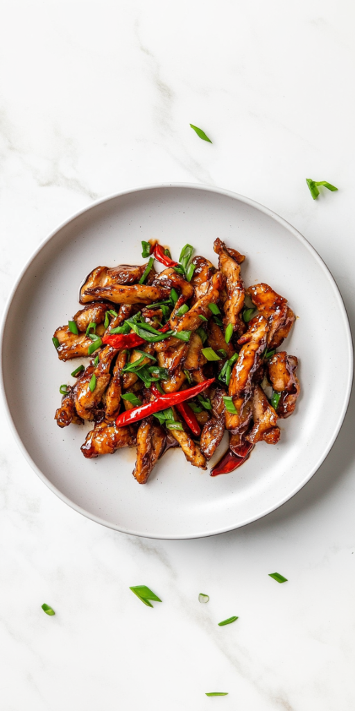 A delicious plate of crispy chilli chicken coated in a glossy, sticky sauce made from soy sauce, honey, and sriracha. The chicken is garnished with fresh chopped spring onions and served on a white ceramic plate placed on a clean white marble countertop, capturing the rich texture and mouthwatering appeal of this Indo-Chinese dish.
