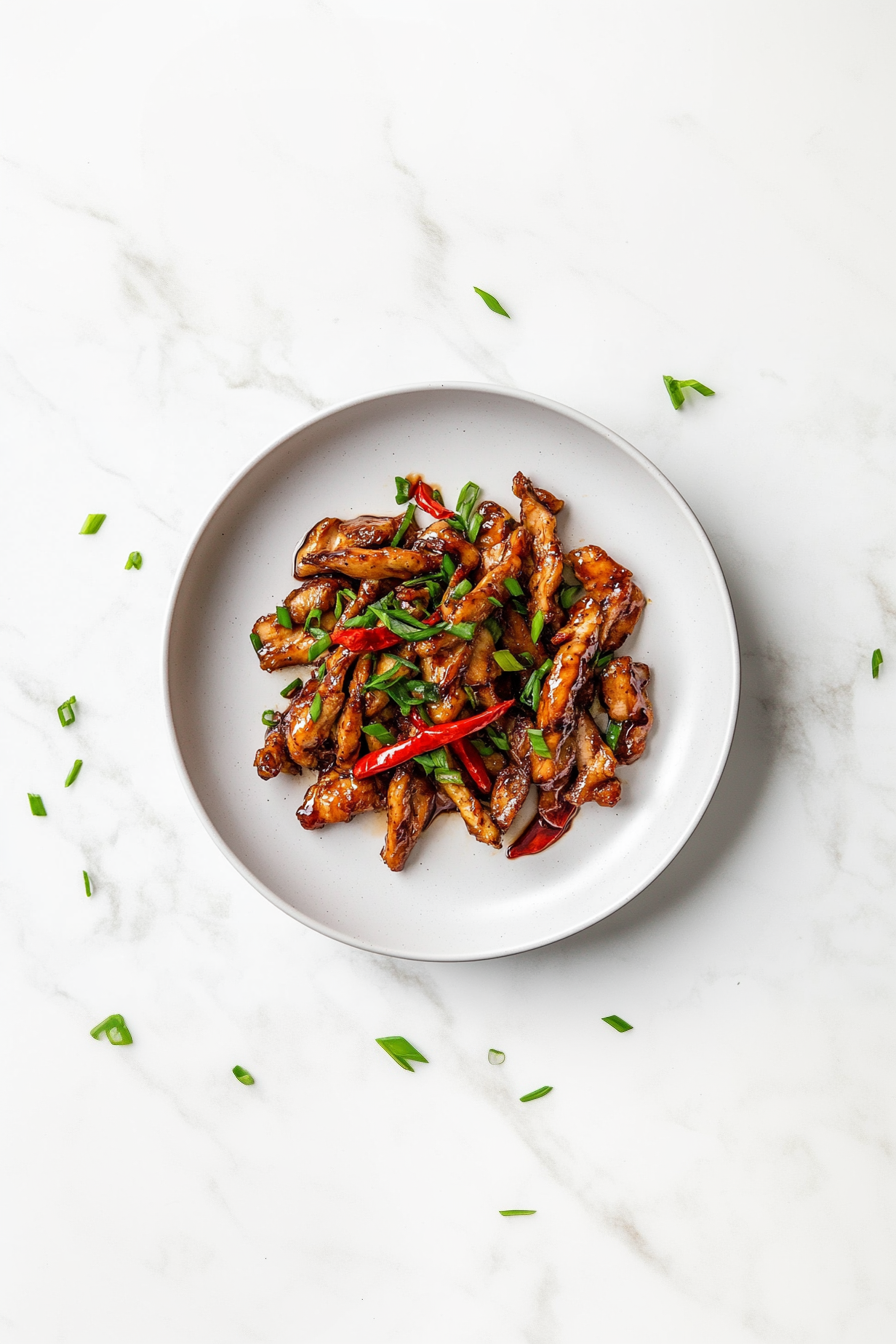 A delicious plate of crispy chilli chicken coated in a glossy, sticky sauce made from soy sauce, honey, and sriracha. The chicken is garnished with fresh chopped spring onions and served on a white ceramic plate placed on a clean white marble countertop, capturing the rich texture and mouthwatering appeal of this Indo-Chinese dish.