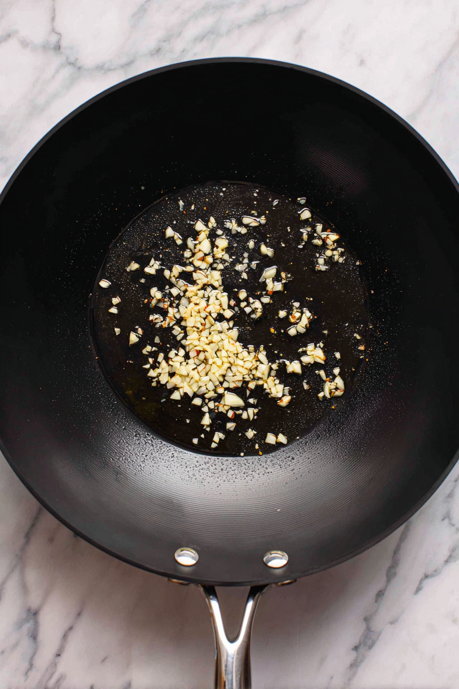 Heat oil in a wok, add chopped garlic, and sauté until fragrant.