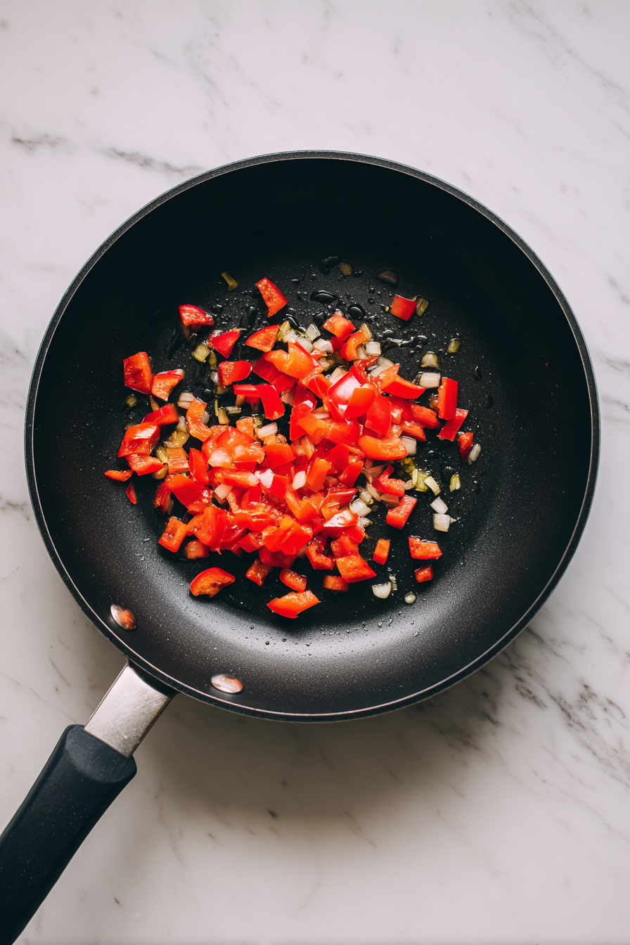 Heat 1 tablespoon oil in a skillet and sauté red bell pepper, jalapeño, and garlic for 2–3 minutes.