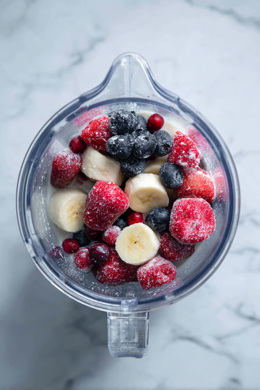Add frozen berries, banana slices, and almond or coconut milk to a blender.