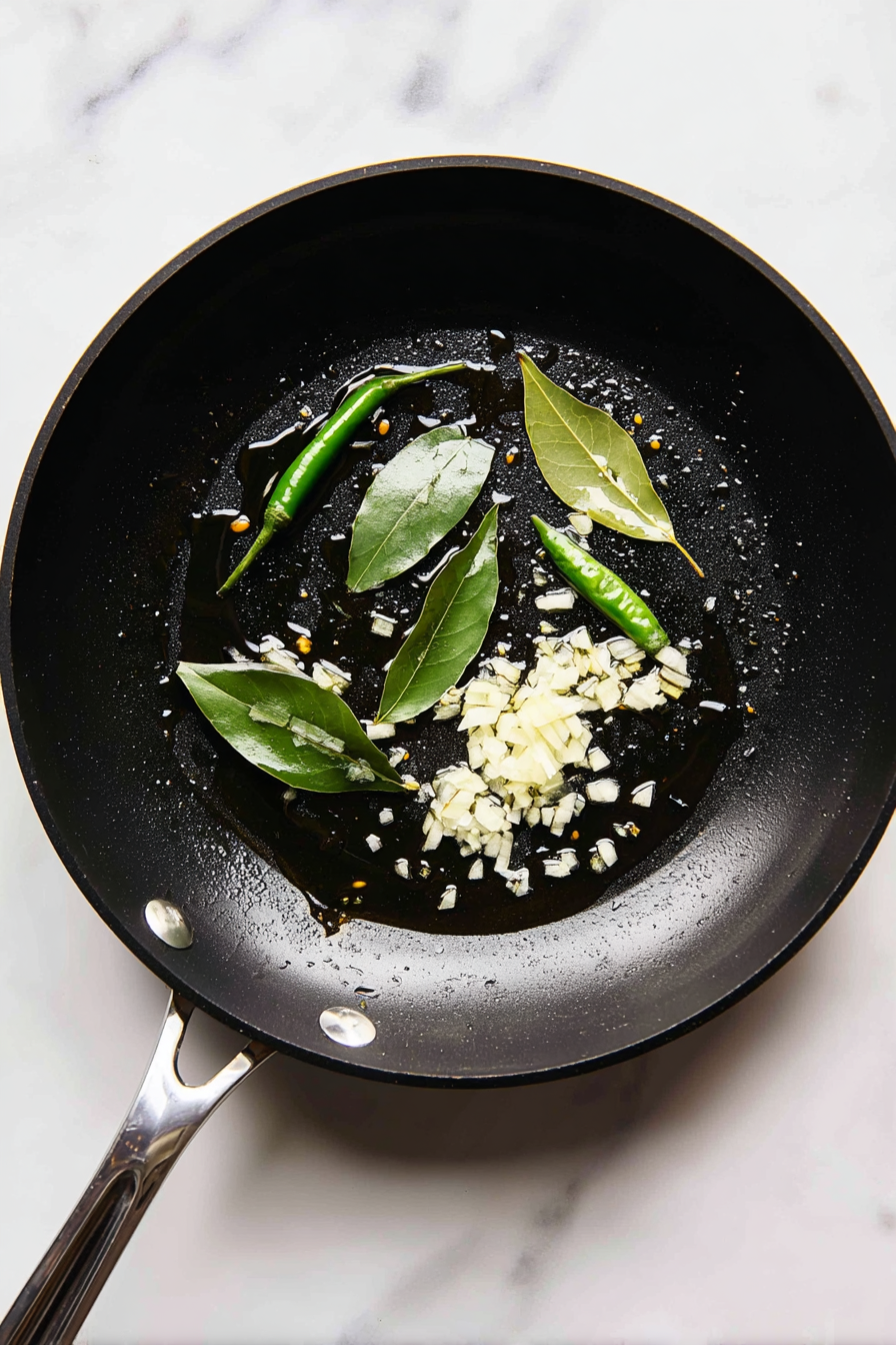 In the same pan, heat more oil and butter, add bay leaf, green chili, and chopped onion.
